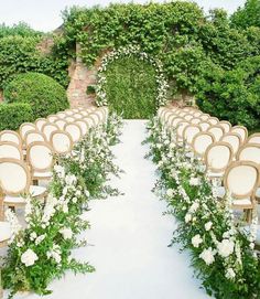 an outdoor ceremony setup with chairs and flowers on the aisle, surrounded by greenery