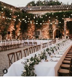 a long table with white linens and greenery is set up for an outdoor dinner