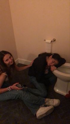 two people sitting on the floor in front of a toilet