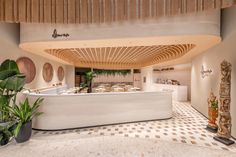 the interior of a restaurant with white counter tops and wooden accents on the ceiling, along with potted plants