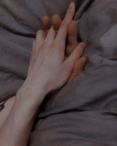 a person's hand resting on top of a bed with gray sheets and pillows