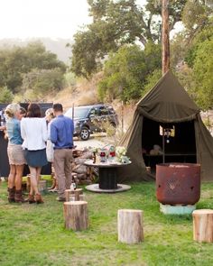 people are standing in the grass near a teepee tent and table with drinks on it