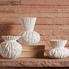 three white vases sitting on top of a wooden shelf next to a brick wall