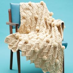 a crocheted blanket sitting on top of a wooden chair next to a blue wall