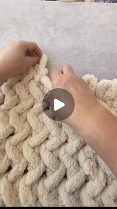 someone crocheting a blanket on top of a bed with another person's hand