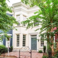 a white house with blue shutters and trees in front of it, surrounded by greenery