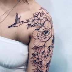 a woman's shoulder with flowers and a humming bird tattoo on her left arm