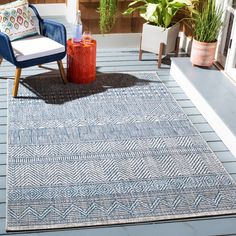 a blue and white area rug on a deck with two chairs, an umbrella and potted plants