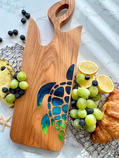 a cutting board with grapes, lemons and croissants next to it