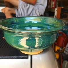 a green bowl sitting on top of a counter next to a person in the background