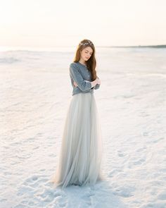 a woman standing in the snow wearing a gray dress and headband with her hands on her hips