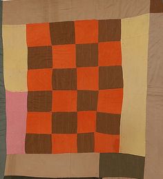 an orange and brown checkered quilt hanging on a wall