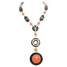 This exquisite necklace embodies timeless elegance and luxurious craftsmanship, meticulously assembled in 18 karat white gold. It features a harmonious blend of polished onyx and vibrant coral beads, seamlessly connected through shimmering diamond links. The centerpiece of this necklace is a striking pendant showcasing an onyx backdrop encircled by a halo of round-cut diamonds, highlighting a central, lustrous coral gem. The coral elements are thoughtfully interspersed throughout the piece, adding a warm, captivating glow that contrasts beautifully with the deep, glossy black of the onyx. Each onyx bead in this necklace is carefully selected for its gloss and uniformity, ensuring a seamless aesthetic flow. Similarly, the coral beads are praised for their smooth texture and rich, consistent Chic Cocktail Dress, Evening Gala, White Gold Pendant Necklace, Onyx Necklace, Elements Of Design, Onyx Bead, Coral Beads, Drop Necklace, Gold Pendant Necklace