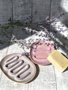 two soap dishes sitting on top of a wooden table next to lavender flowers and a bar of soap