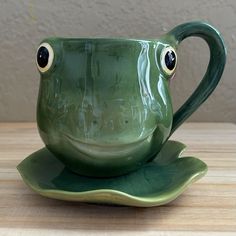 a green coffee cup with two eyes and a leaf shaped saucer on a wooden table