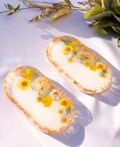 two yellow and white plates with flowers on them sitting on a table next to plants