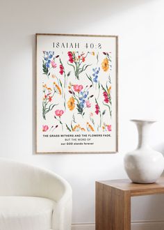 a white vase sitting on top of a wooden table next to a wall mounted poster