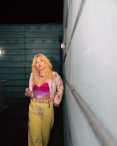 a woman standing next to a wall wearing yellow pants