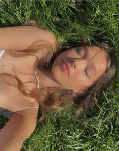 a woman laying in the grass with her eyes closed and head tilted to the side