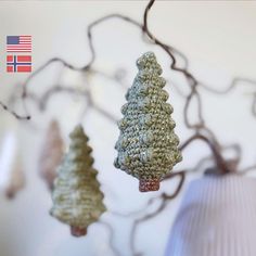 three crocheted christmas trees hanging from a tree branch with the american flag in the background