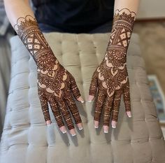 two hands with henna designs on them sitting on top of a cushioned surface