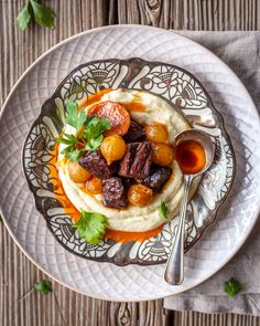 a white plate topped with mashed potatoes and carrots next to a silver spoon