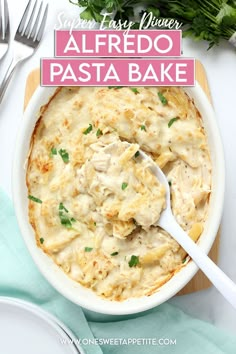 a white bowl filled with alfredo pasta on top of a wooden cutting board next to silverware