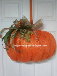 an orange pumpkin hanging from the front door with ribbon and bows on it's head