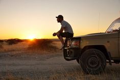 a man sitting on the back of a pick up truck in front of a sunset