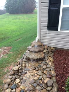 there is a small waterfall in the middle of this rock garden bed that's built into the side of a house