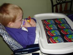 a young boy sitting in a chair with a cell phone to his ear and chewing on a gummy bar