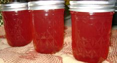 three jars filled with red liquid sitting on top of a cloth covered table next to a stove