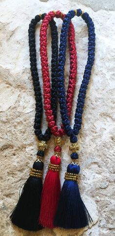 three tasseled necklaces with red, blue and black beads hanging on a stone wall