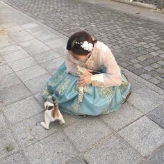 a woman in a blue dress sitting on the ground next to a small white and brown cat