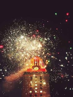 fireworks are lit up in the night sky above a building with a clock on it