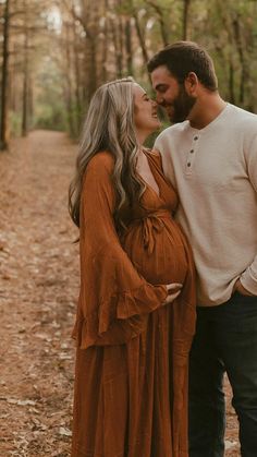 a pregnant couple kissing while standing in the woods