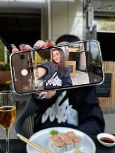 a woman taking a selfie with her cell phone while eating sushi and chopsticks