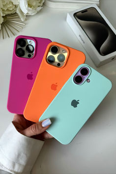 four different colored iphone cases sitting next to each other on a white table with flowers in the background