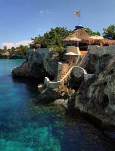 the water is crystal blue and there are umbrellas in the shade on the rocks