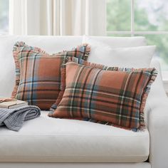 two plaid pillows on a white couch with a blanket next to it and a book