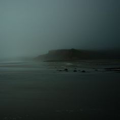 a foggy day at the beach with an island in the distance