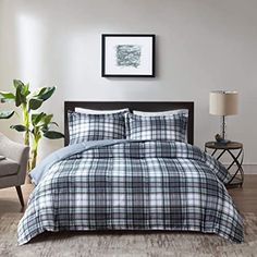 a bed in a room with a plaid comforter and pillows on the floor next to a chair