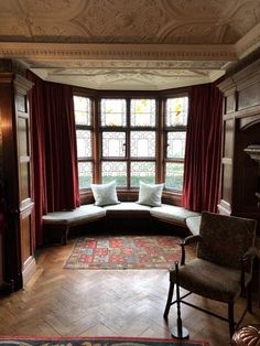 a living room filled with furniture next to a window covered in red curtains and drapes