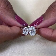 a woman's hands with pink manicured nails holding two diamond shaped engagement rings