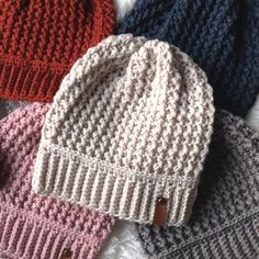 four knitted hats laying on top of each other in different colors and sizes, all with buttons