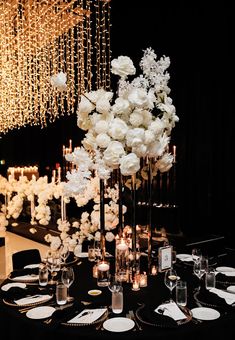 a black table topped with lots of white flowers next to tall candles and chandeliers