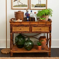 a table with vases, plants and pictures on the wall above it in a living room