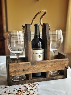 two wine glasses and a bottle in a wooden crate on a table with white linens