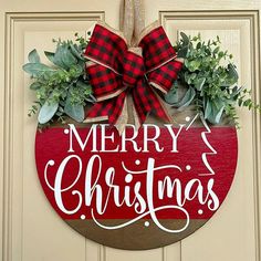 a merry christmas sign hanging on a door with red and black plaid bow around it