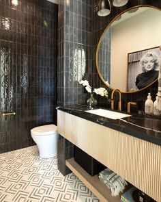 a black and white tiled bathroom with a gold framed mirror above the sink, along with a toilet